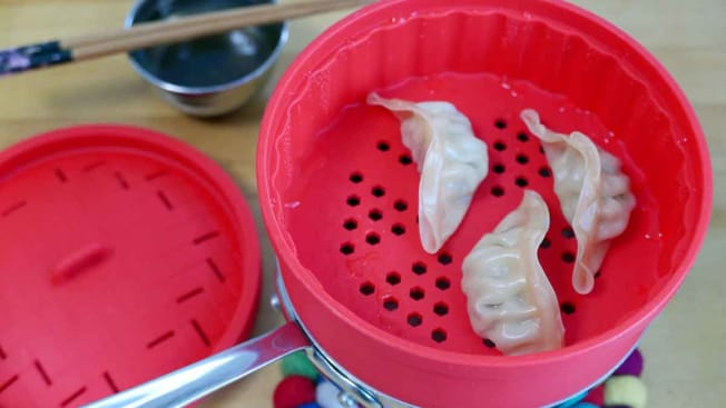 overhead view of red silicone steamer on top of pot with dumplings in steamer